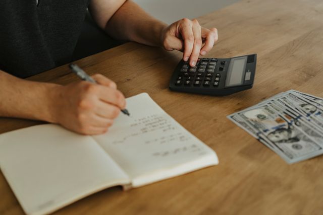 hands using a calculator with notebook and cash on a wooden table